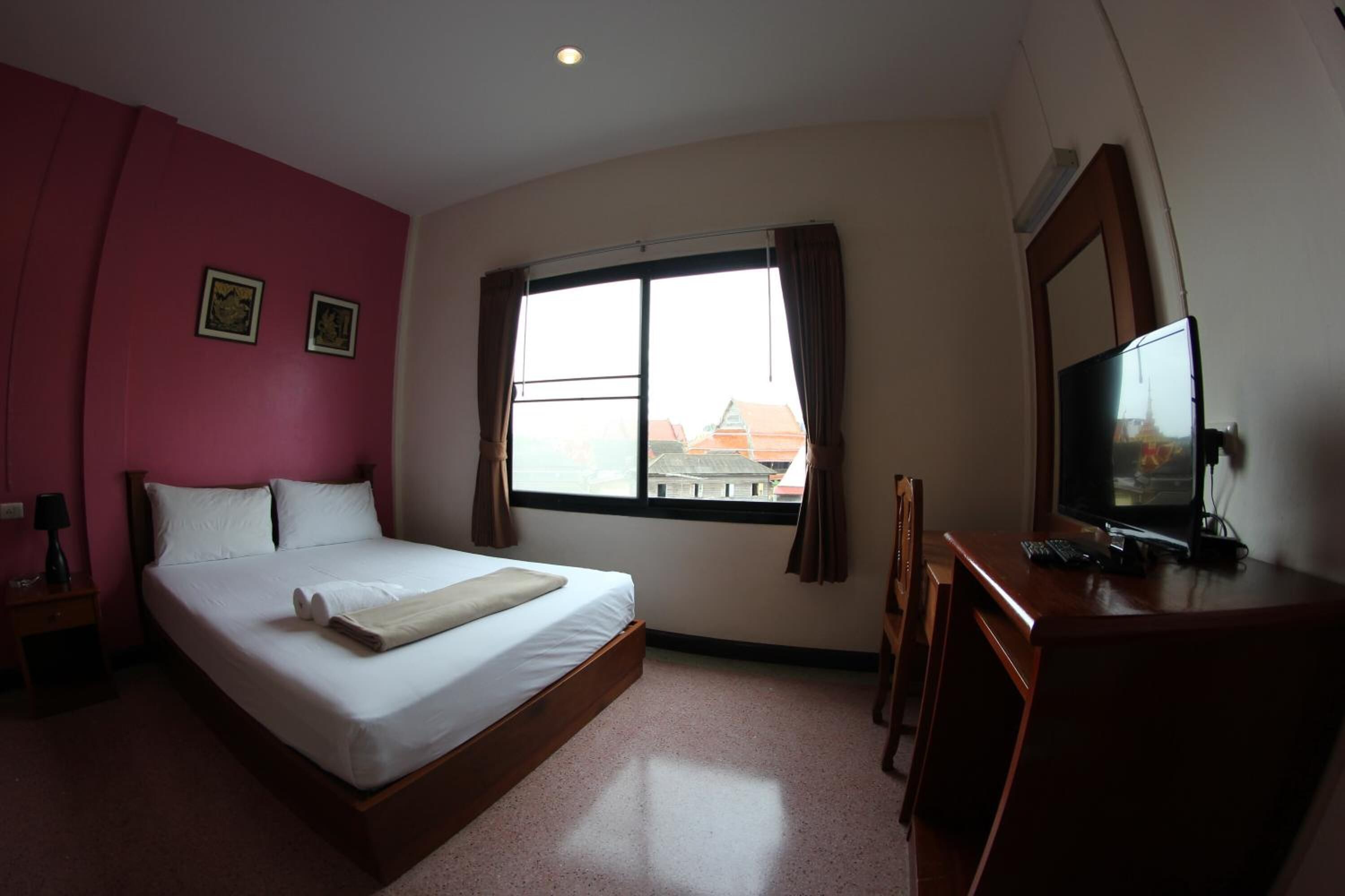 Una habitación de hotel con una cama, un escritorio con televisor, una ventana con cortinas y vistas a edificios.