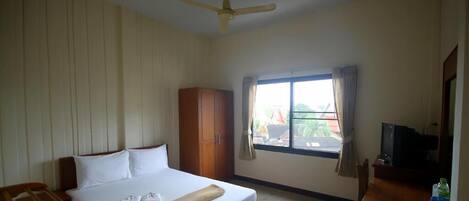 Habitación de hotel con cama, armario de madera, escritorio con televisor y ventana con cortinas.