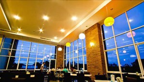 Un restaurant doté de grandes fenêtres, d’un éclairage intérieur et de tables.