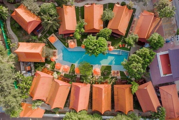 Vista aèria d'un complex turístic amb diversos edificis de tipus bungalot, una piscina central i vegetació al voltant.