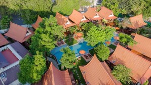 Vista aérea de un complejo turístico con varias construcciones, una piscina central y abundante vegetación.