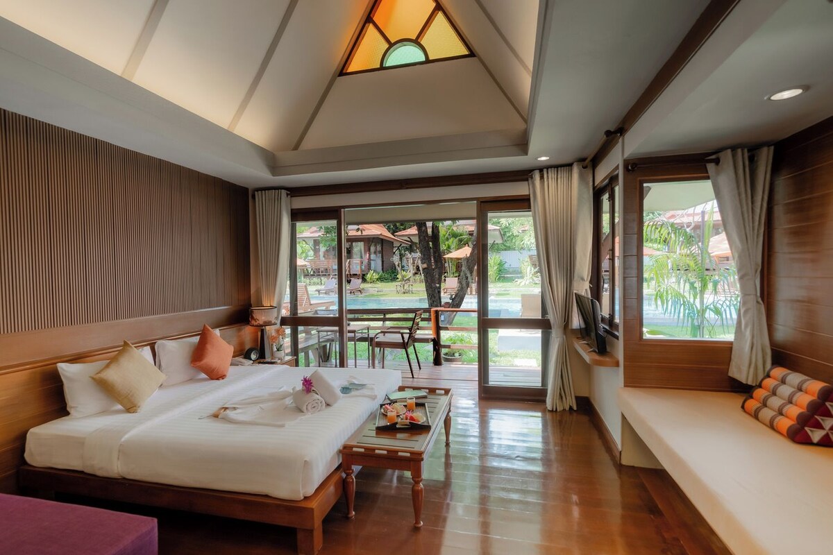 Habitación de hotel con cama, una mesita, televisión y vista a la piscina y el jardín.