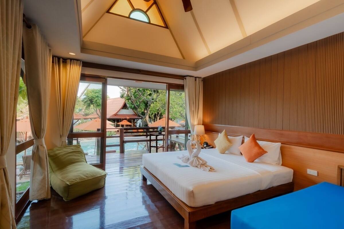 A hotel room with a large bed, a small sofa, a wooden headboard, and a view of an outdoor pool area.