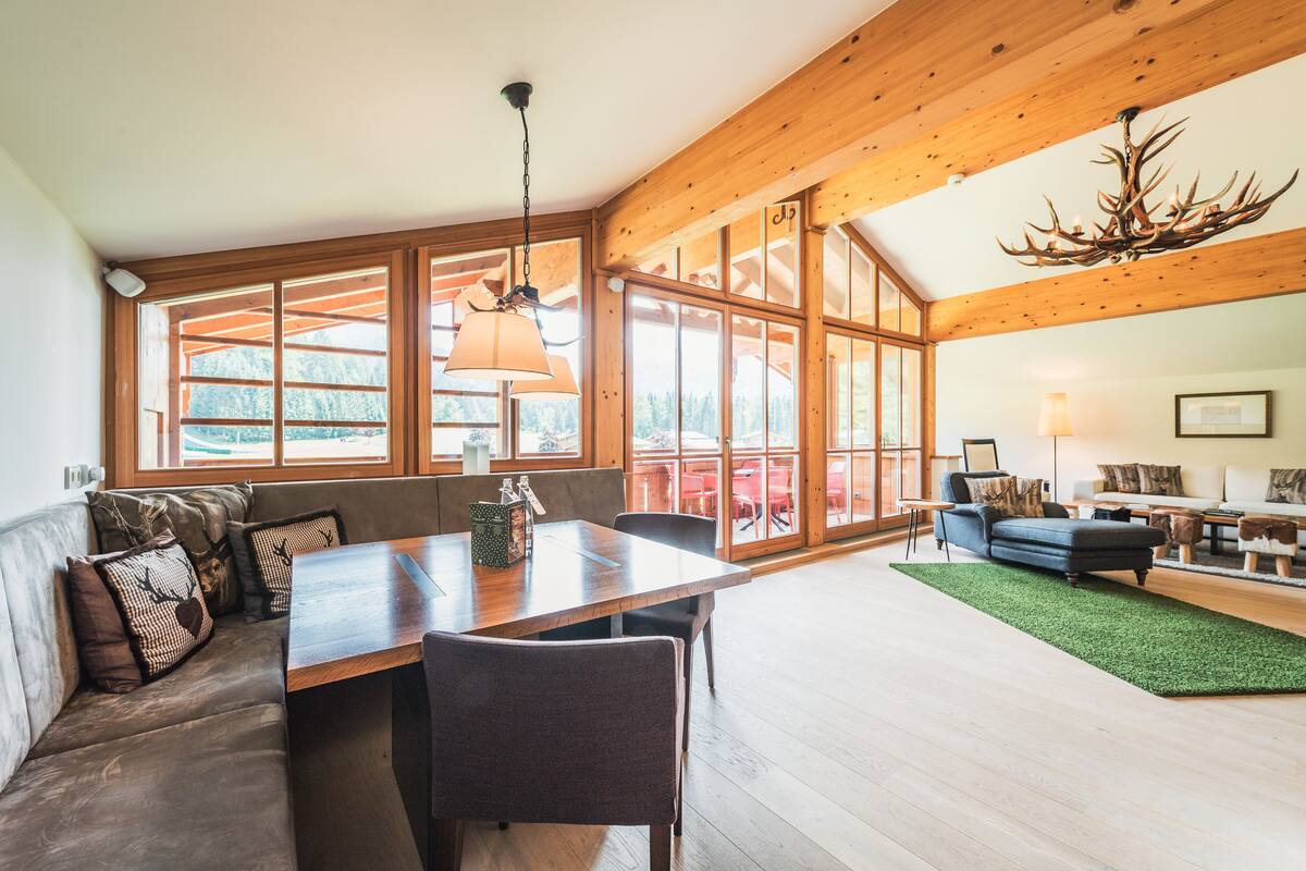 Amplia sala de estar con techo de madera, ventanas grandes y una mesa de comedor con sillas.