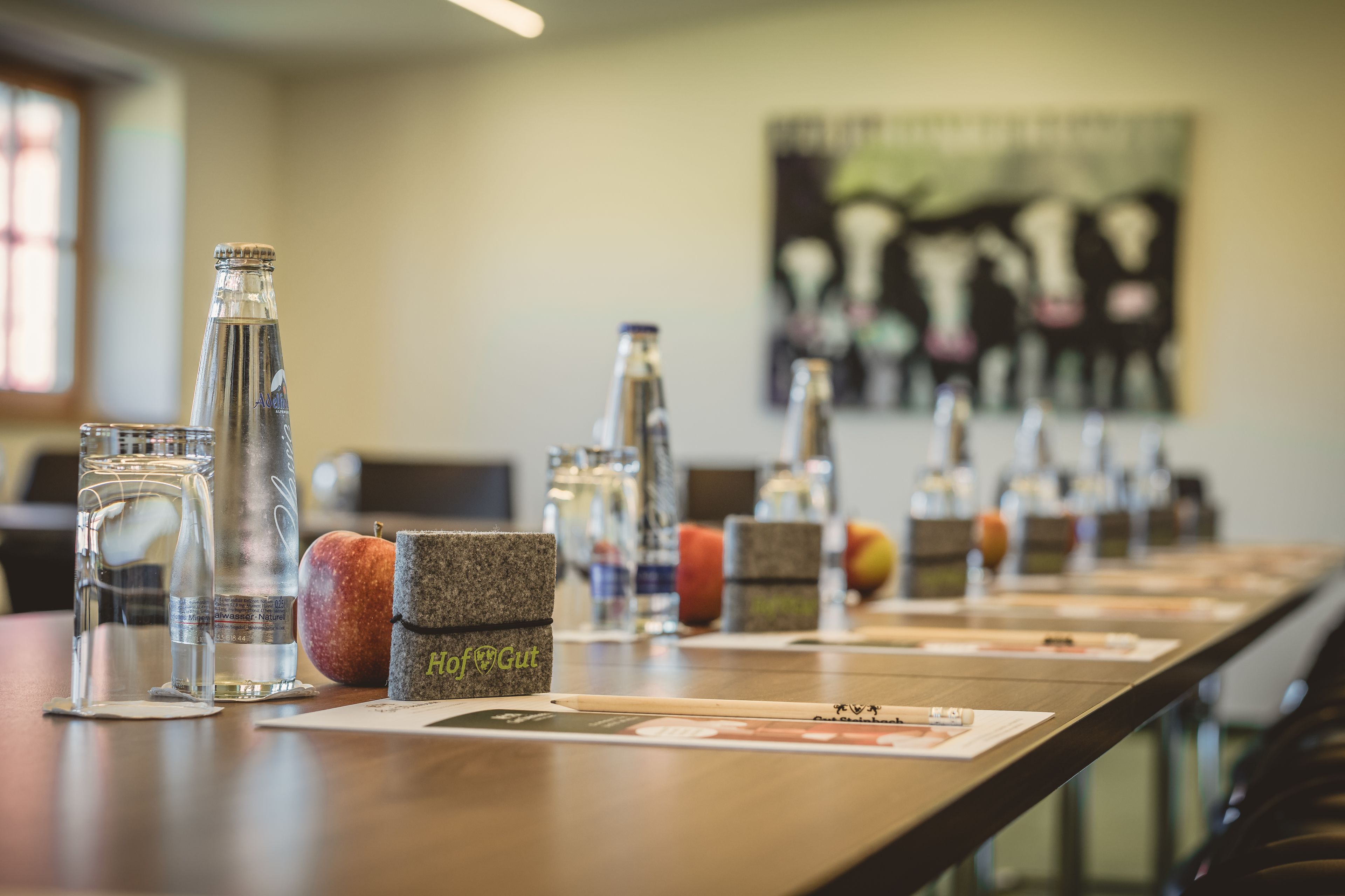 Una larga mesa con botellas de agua, un vaso y un frutero.