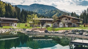 Eine Holzhütte am Seeufer mit einer Anlegestelle, umgeben von Wald und Bergen.