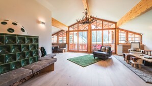 Ein geräumiges Wohnzimmer mit hoher Decke, Holzbalken, einem großen Fenster und einem grünen Teppich.