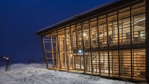 Ein modernes Gebäude mit großen Glasfenstern und einer Holzfassade, umgeben von Schnee.