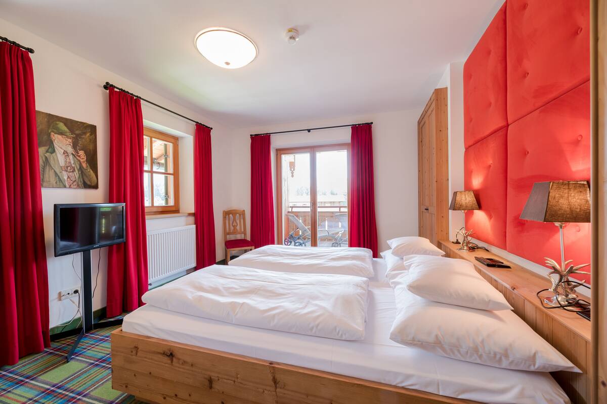 Una habitación de hotel con una cama, cortinas rojas, un televisor, una ventana y un cabecero rojo.