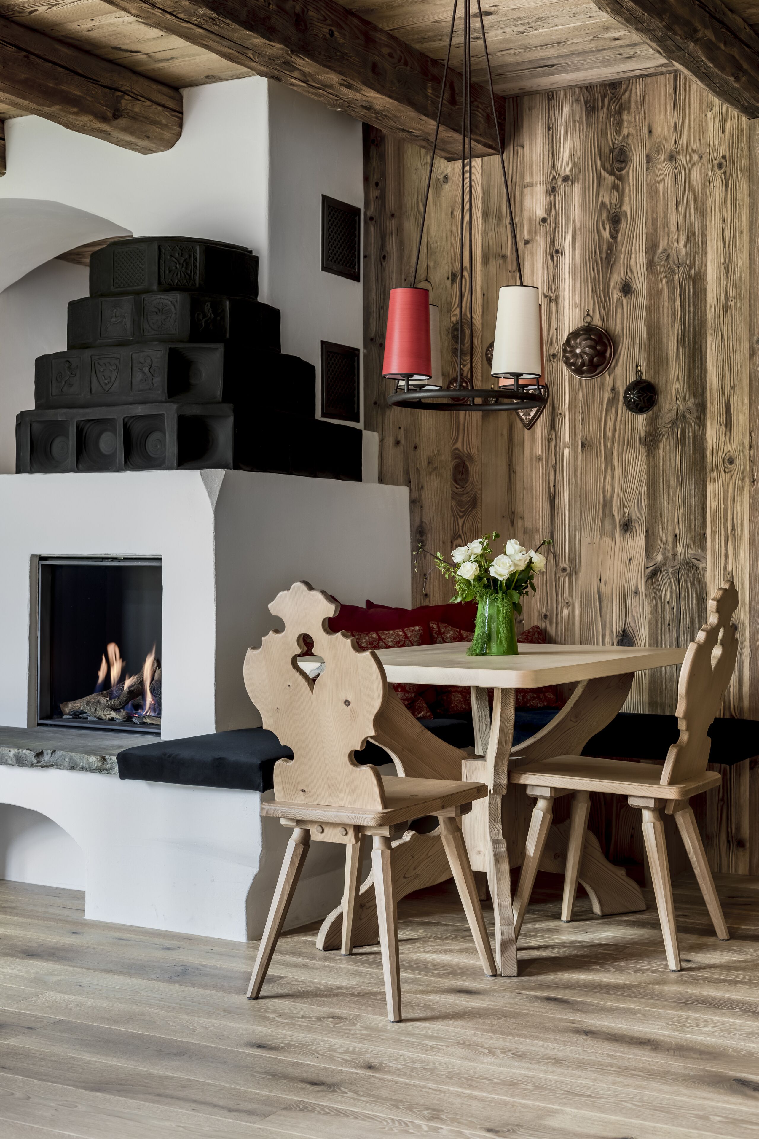 Une pièce chaleureuse avec une cheminée, des murs en bois, une table à manger avec des chaises et un vase rempli de fleurs.