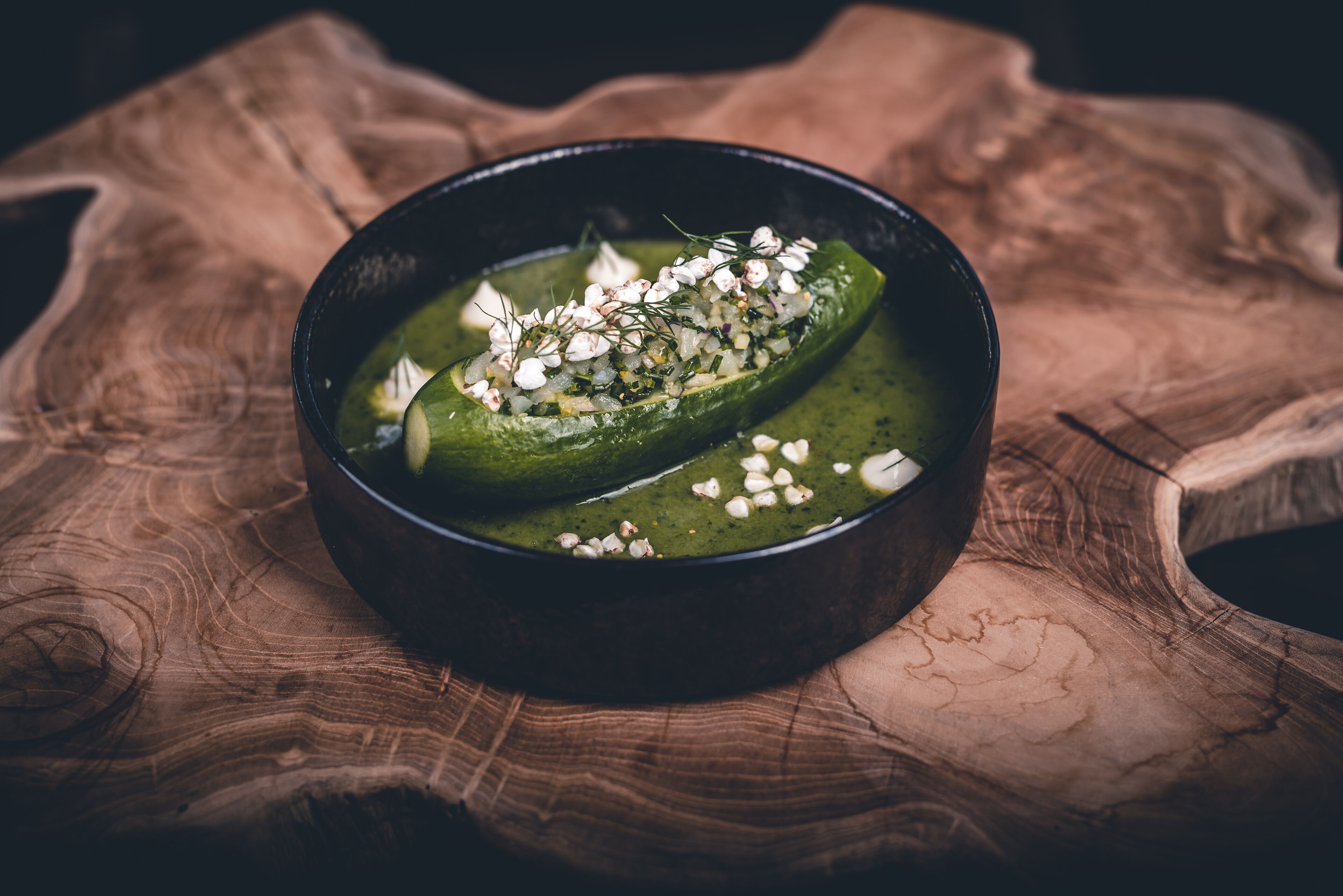 Un bol de soupe verte, garni d’herbes et de fromage, posé sur une surface en bois.