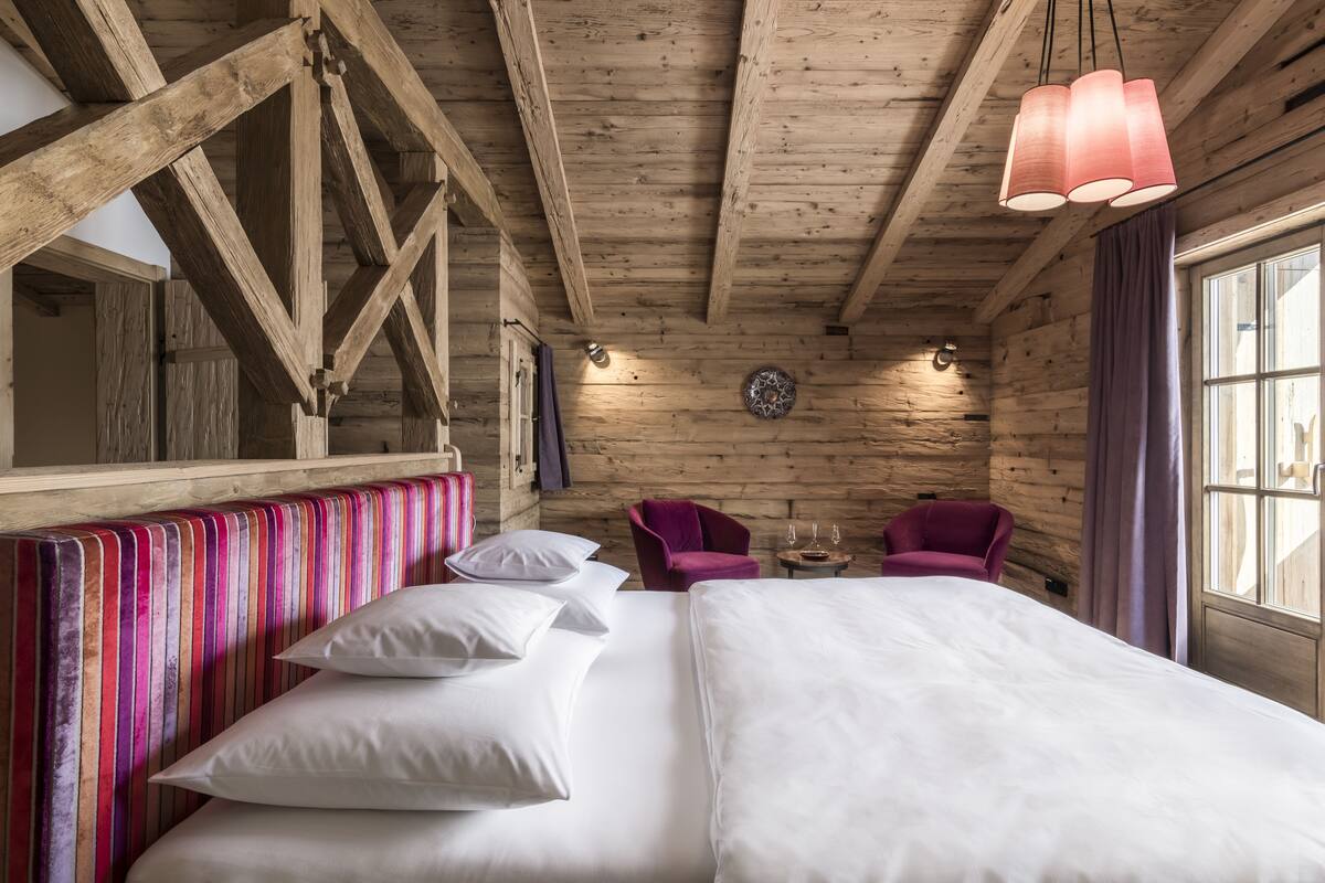 Una habitación tipo cabaña de madera con una cama, dos sillas y una mesita.