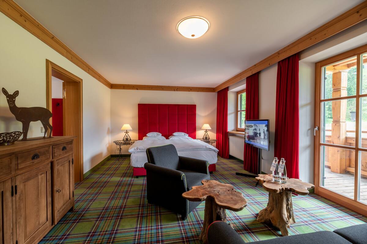 Una habitación de hotel con cama, escritorio, silla, televisión y ventana con cortinas.