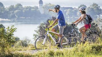 Two people on bicycles on a grassy path with a body of water and a building in the background.