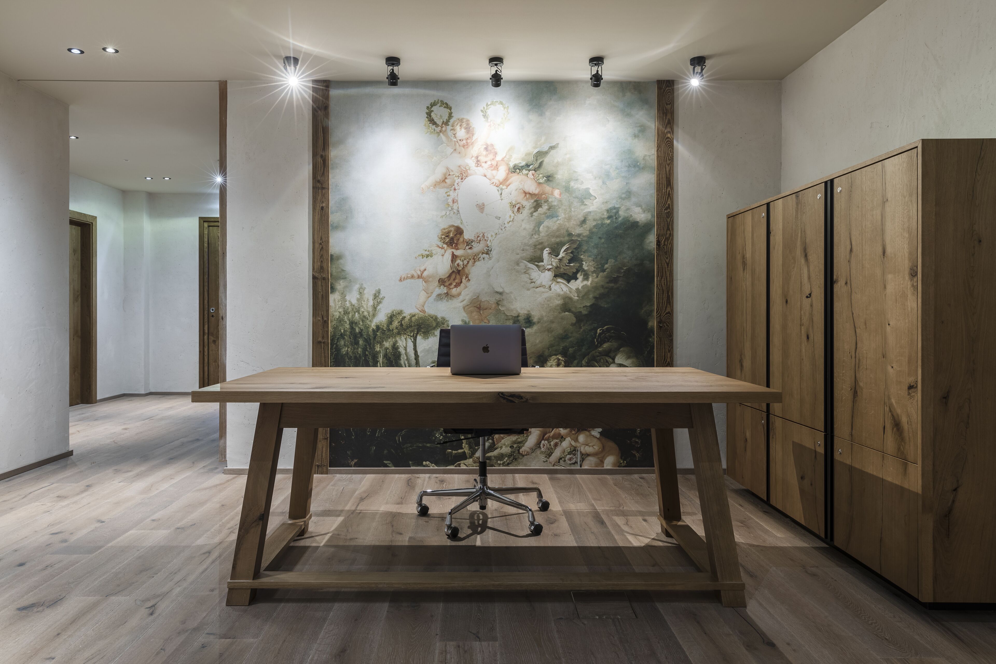 A modern room with a wooden table, a laptop, and a large mural on the wall.