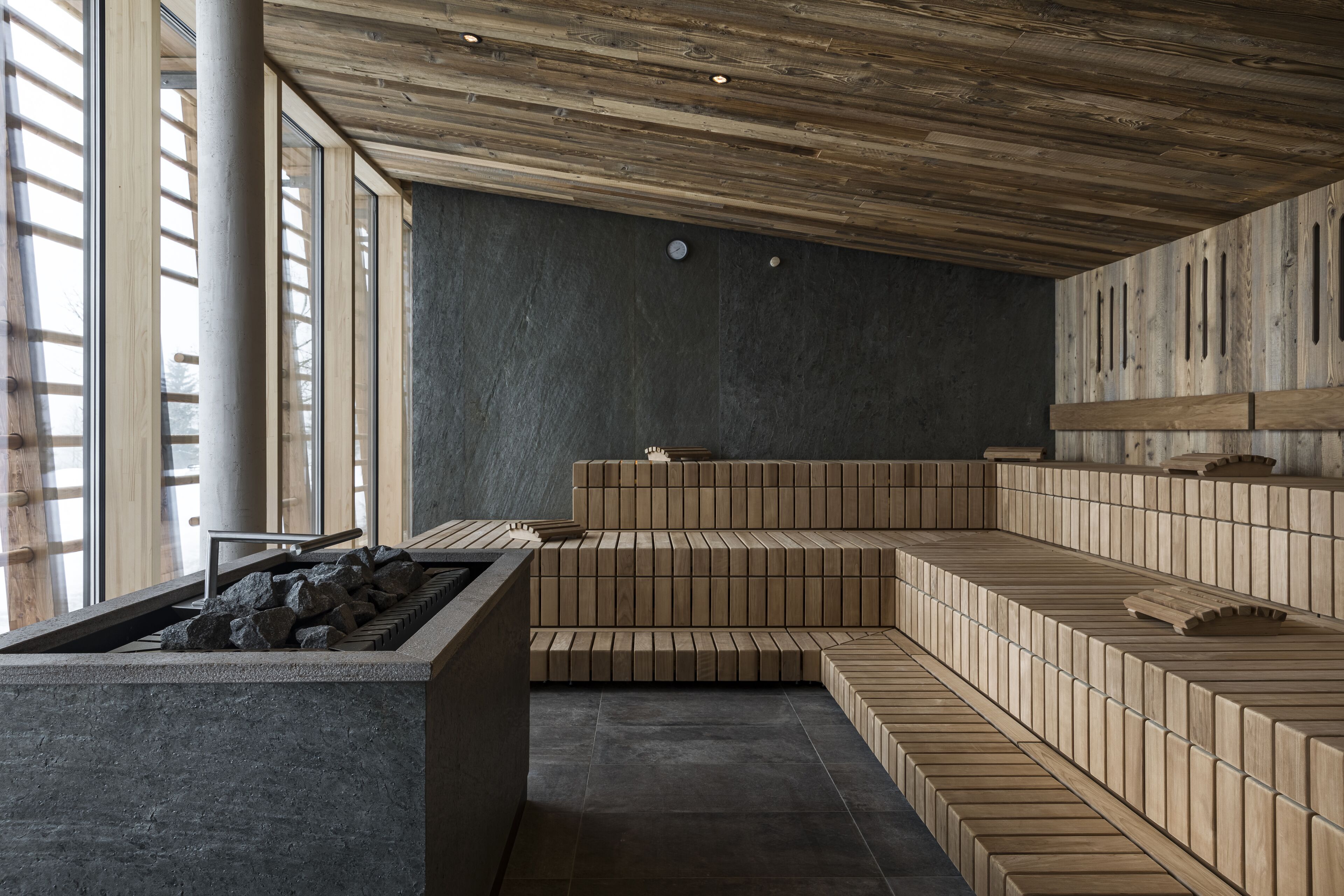 A modern interior with a stone bench, wooden seating, and large windows.