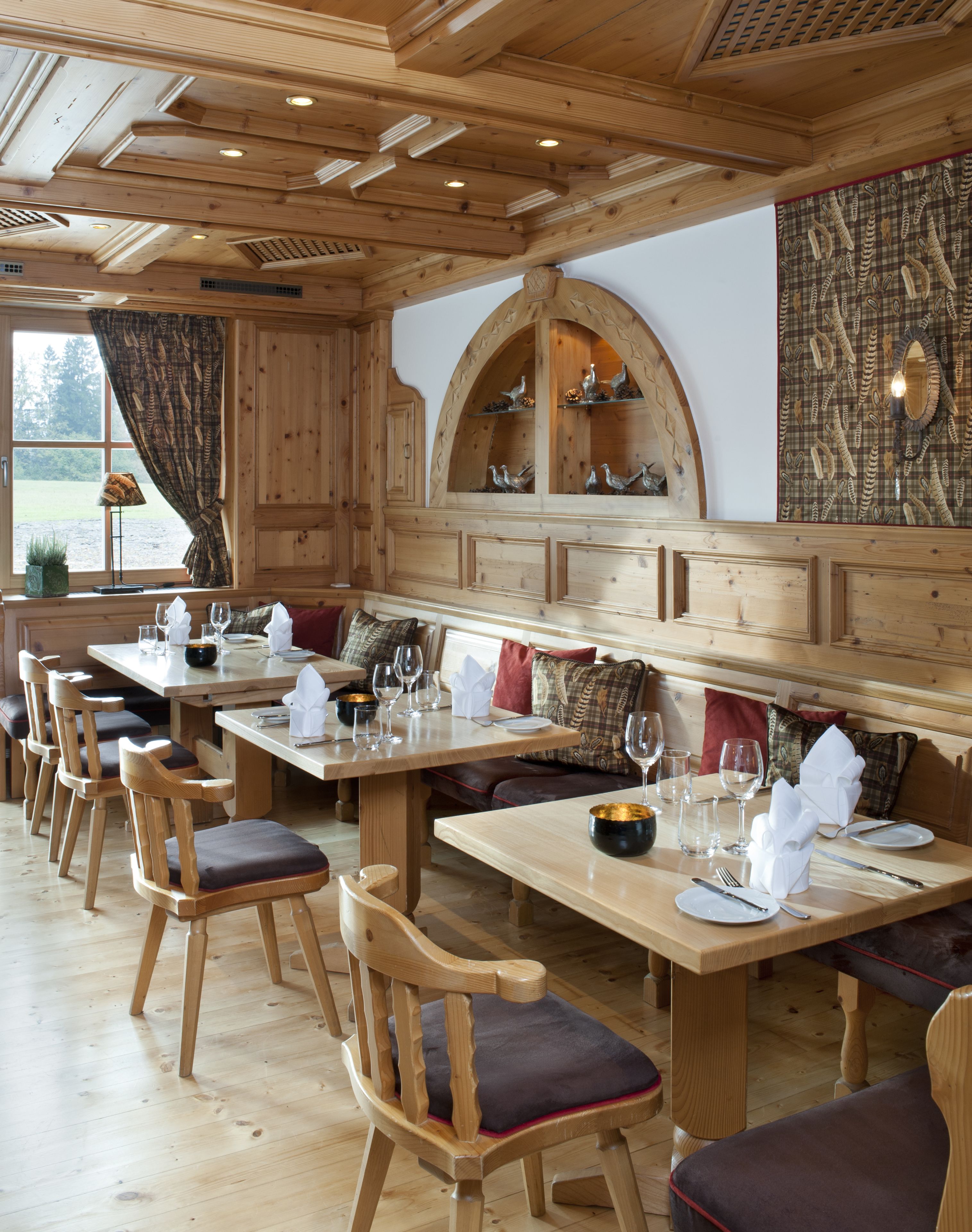 Un coin repas en bois, avec des tables et des chaises, un banc et un mur décoratif orné de motifs d’oiseaux.