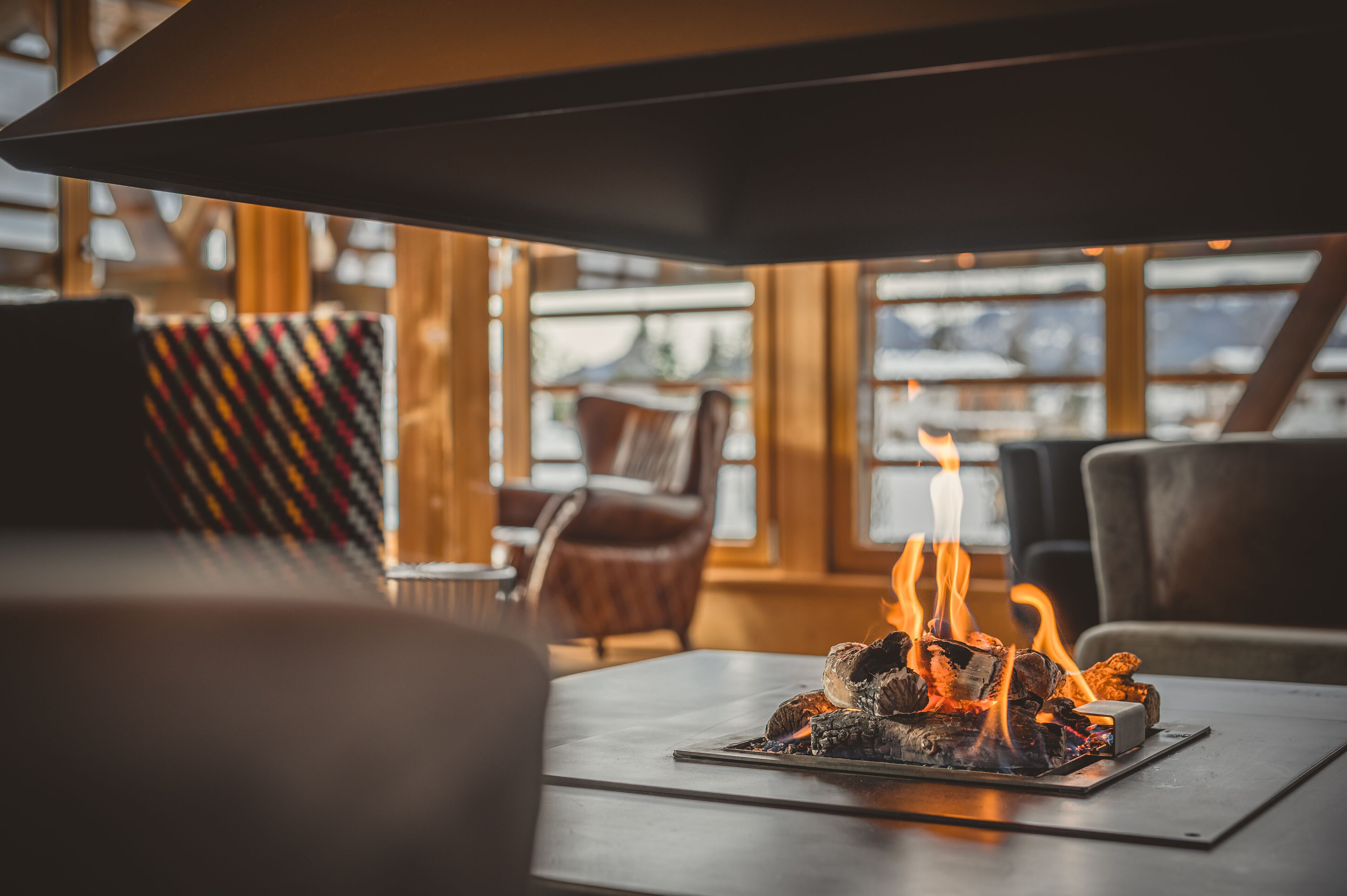 A cozy indoor seating area with a wood-burning fireplace, leather chairs, and large windows.