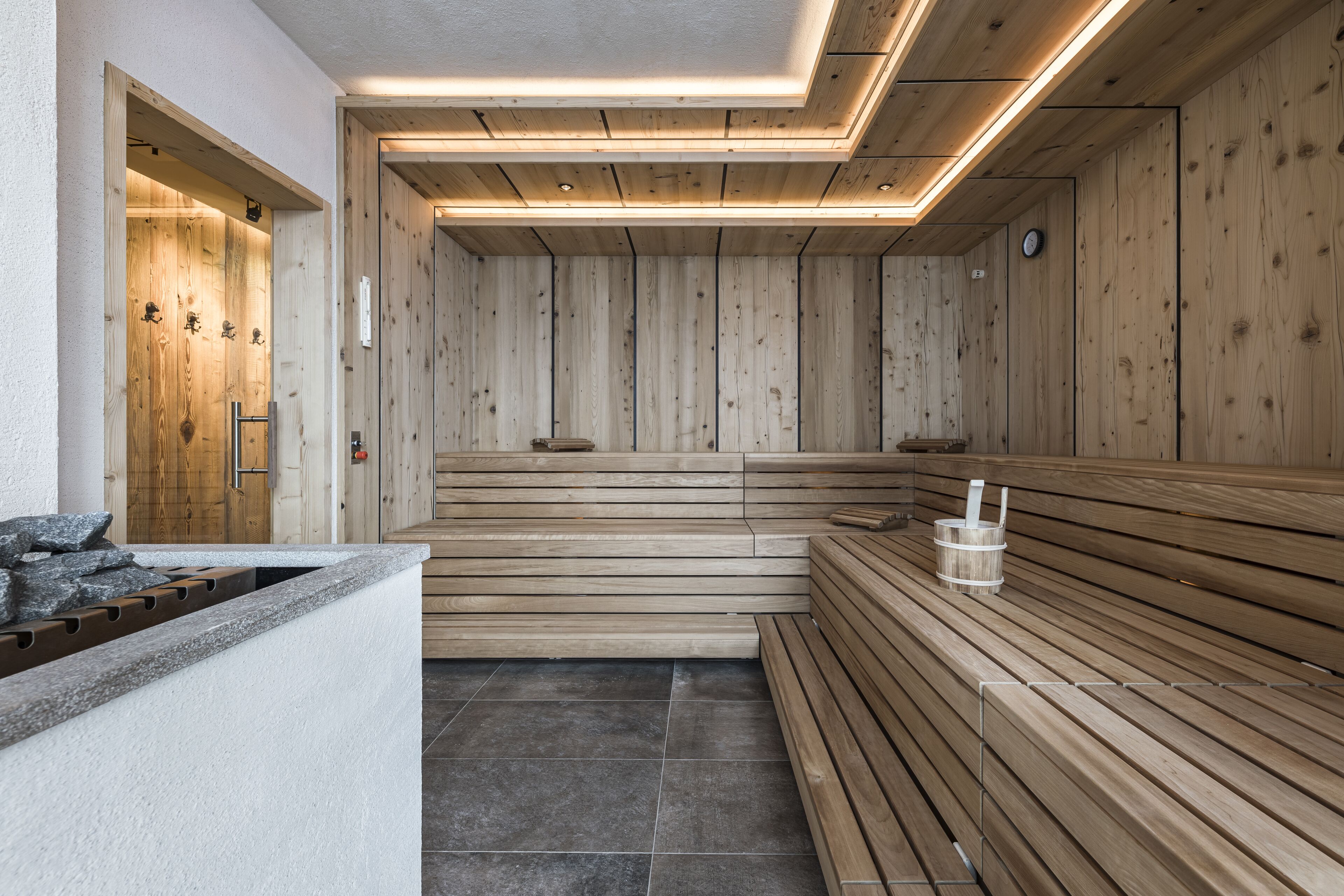 Un sauna avec des bancs en bois et un banc en pierre, une porte en bois et un sol carrelé.