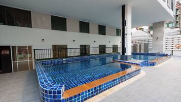 A modern indoor swimming pool with blue tiles and a separate shallow area, surrounded by a covered walkway.