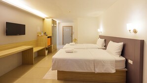 A hotel room with two beds, a TV, a wooden bench, and a small desk.