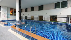 A modern indoor swimming pool with blue tiles, a wooden deck, and a white exterior wall.