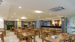 A spacious dining area with multiple wooden tables and chairs, a green wall with a floral mural, and a wall-mounted clock.