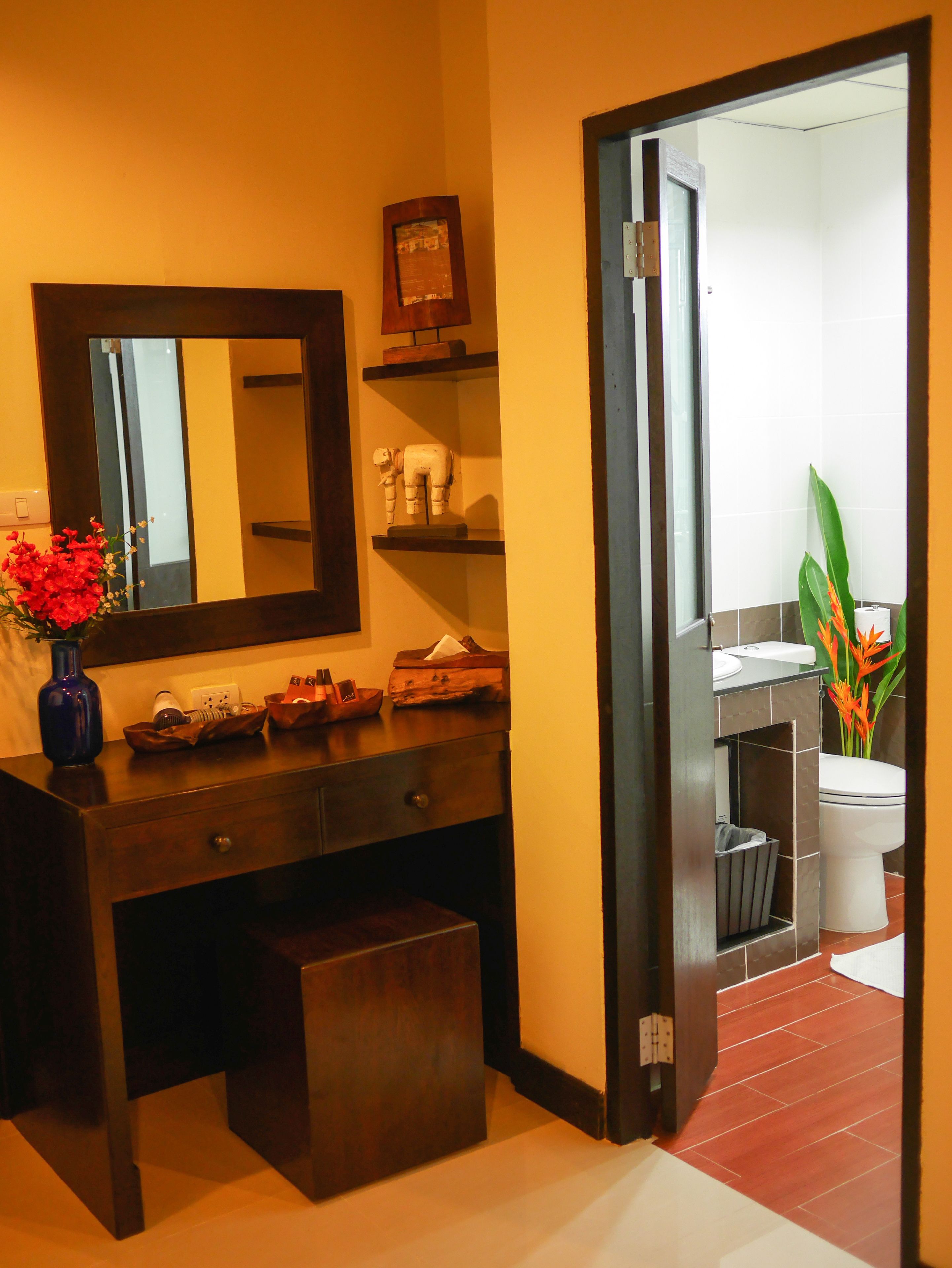 A modern bathroom with a dark wooden vanity, a large mirror, and a toilet visible through an open door.