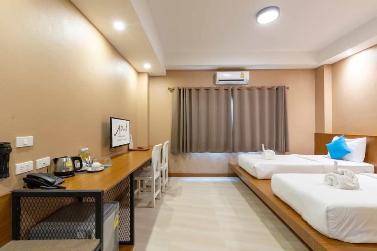 A hotel room with two beds, a desk, a chair, a TV, and an air conditioning unit.