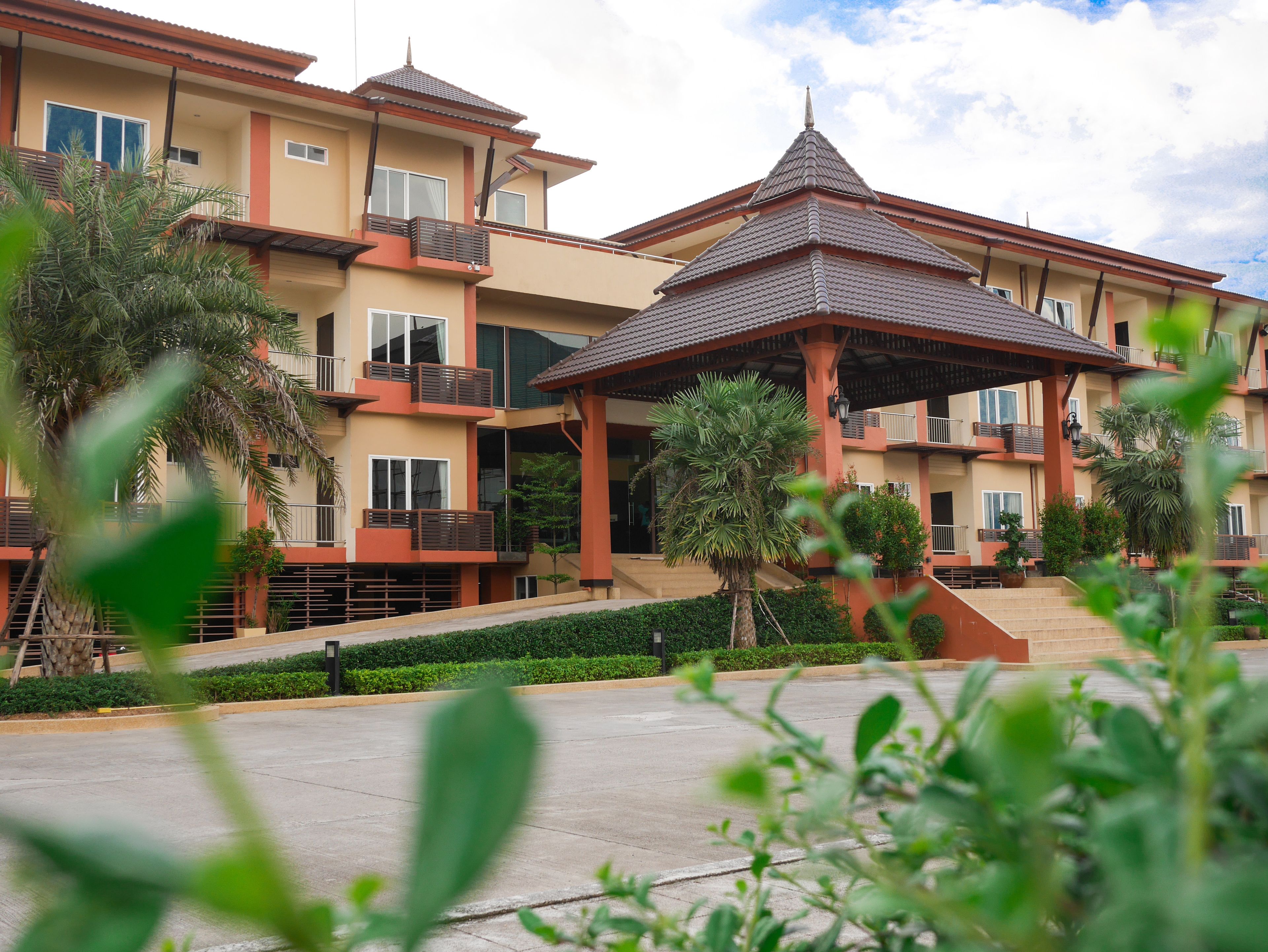 Un hotel de varios pisos con balcones, un pabellón cubierto y un patio ajardinado.