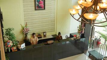 A reception area with a reception desk, two staff members, a framed picture on the wall, and a chandelier.