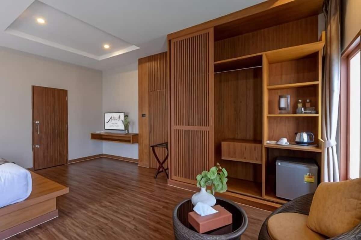 Hotellihuoneessa on sänky, oleskelualue, vaatekaappi ja pieni pöytä, jonka päällä on kasvi.