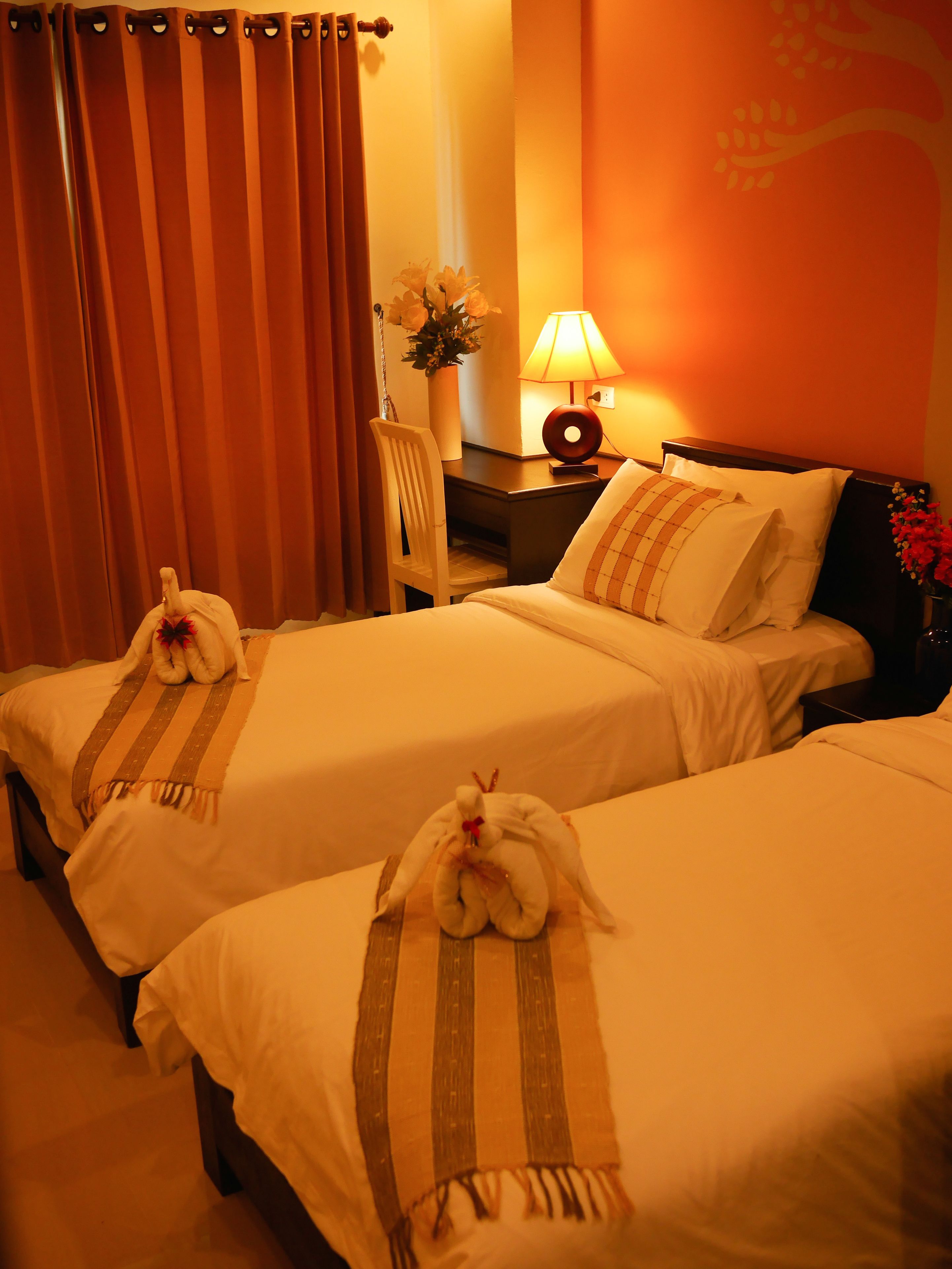 Una habitación de hotel con dos camas, un escritorio, una silla, una lámpara y un florero con flores.