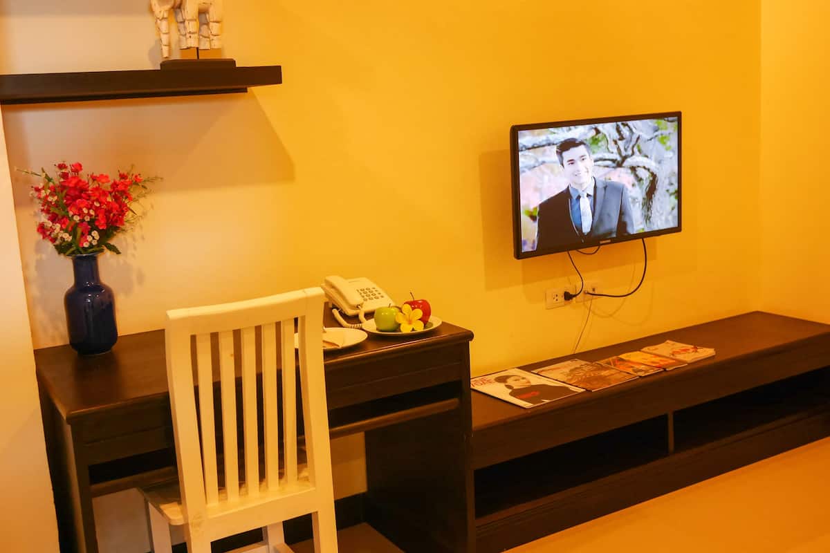 Hotellihuone, jossa on työpöytä, tuoli, maljakko kukkineen, puhelin, televisio ja hylly koriste-esineitä varten.