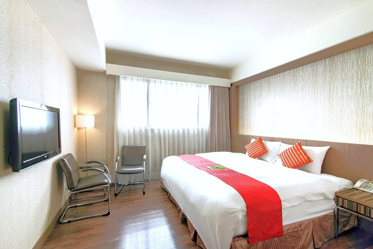 Une chambre d’hôtel avec un grand lit, un téléviseur fixé au mur, une chaise et un bureau avec un téléphone.