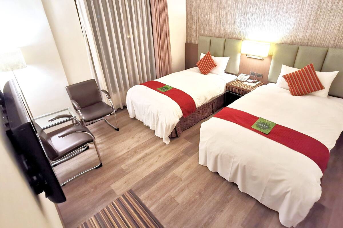 Une chambre d’hôtel avec deux lits, une chaise, un bureau et une lampe.