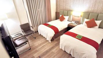 A hotel room with two beds, a chair, a desk, and a lamp.