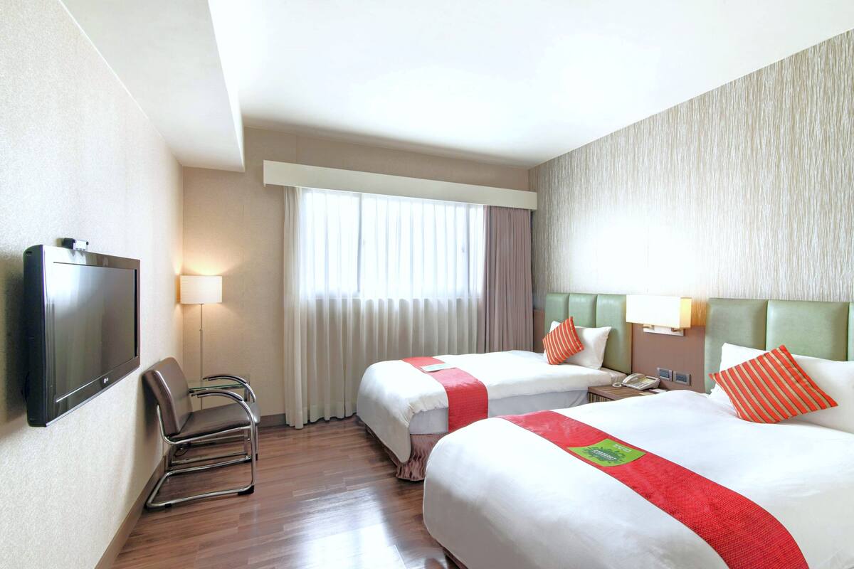 Une chambre d’hôtel avec deux lits, une télévision, une chaise et une fenêtre avec des rideaux.