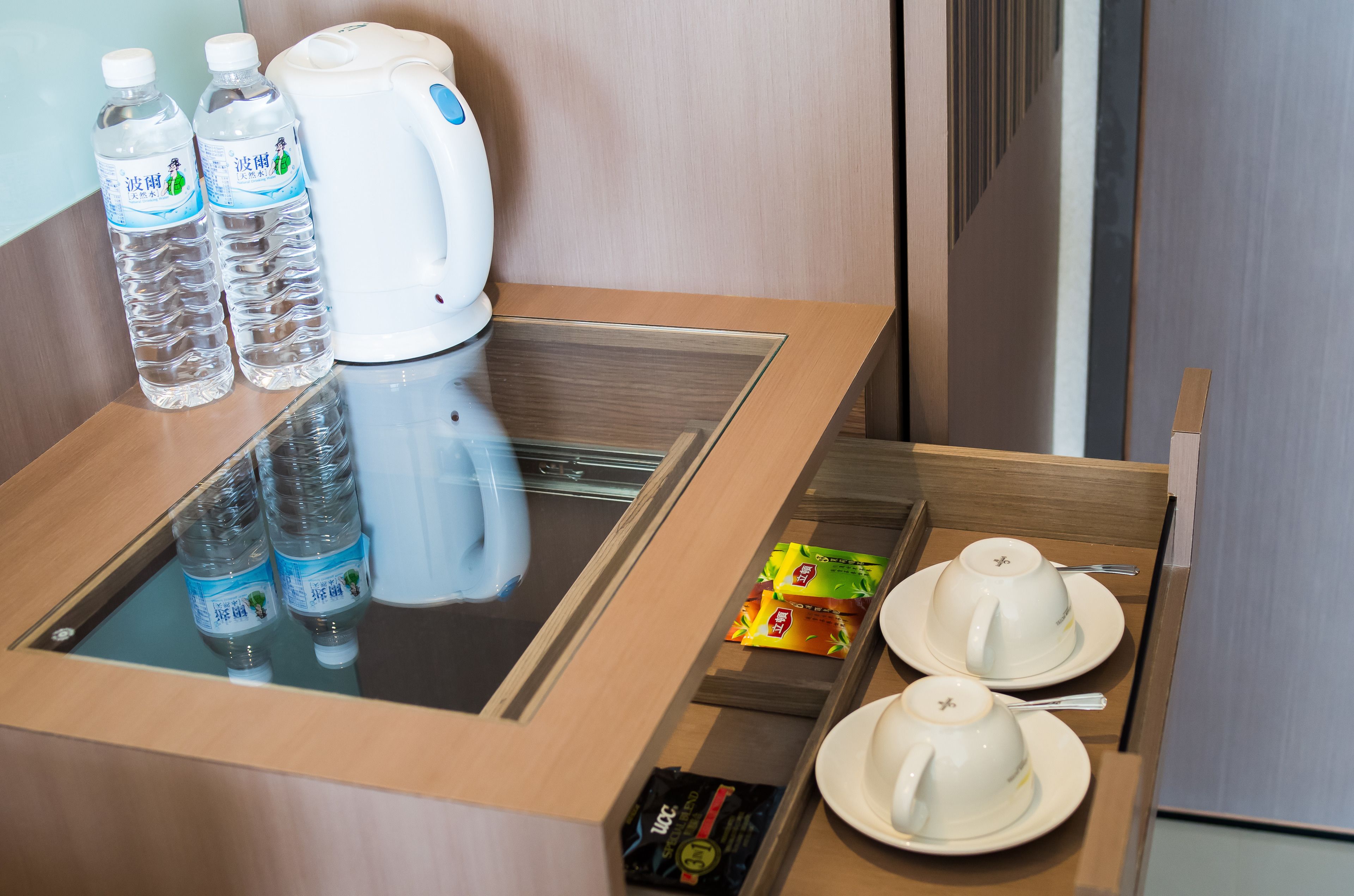 A hotel room with a minibar containing bottled water, a coffee maker, tea packets, and teacups.