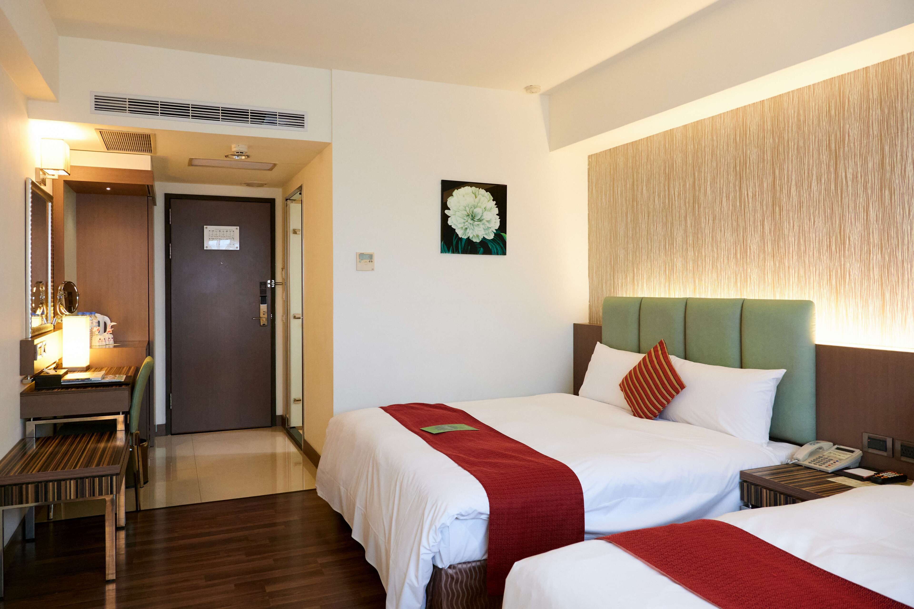 A hotel room with two beds, a desk with a chair, a telephone, and a wall-mounted artwork.