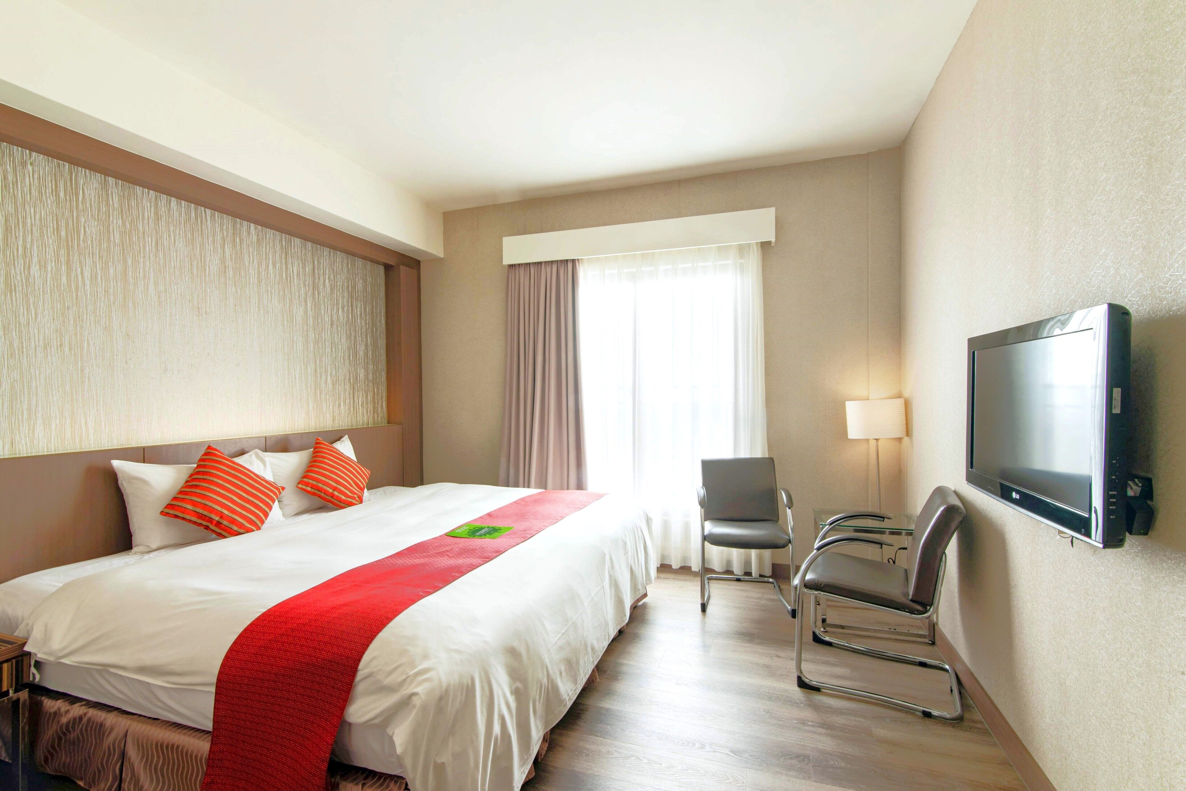 A hotel room with a large bed, a TV, a chair, and a window with curtains.