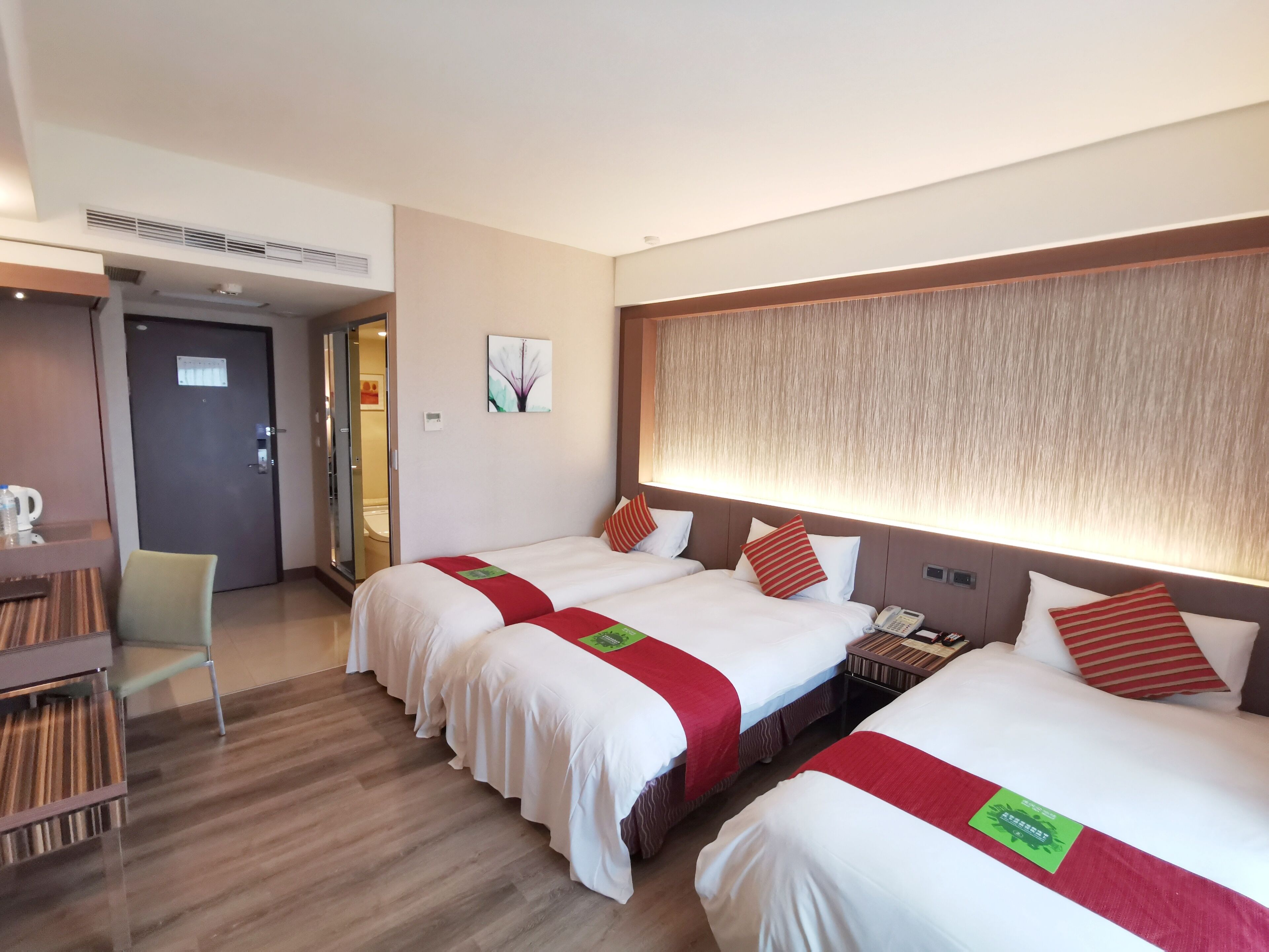 Une chambre d’hôtel avec trois lits, un bureau en bois et une chaise.