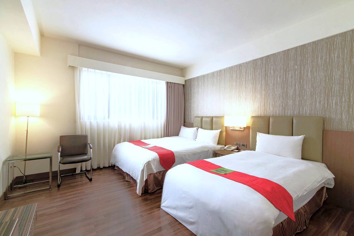 Une chambre d’hôtel avec deux lits, une chaise, un bureau et une lampe.