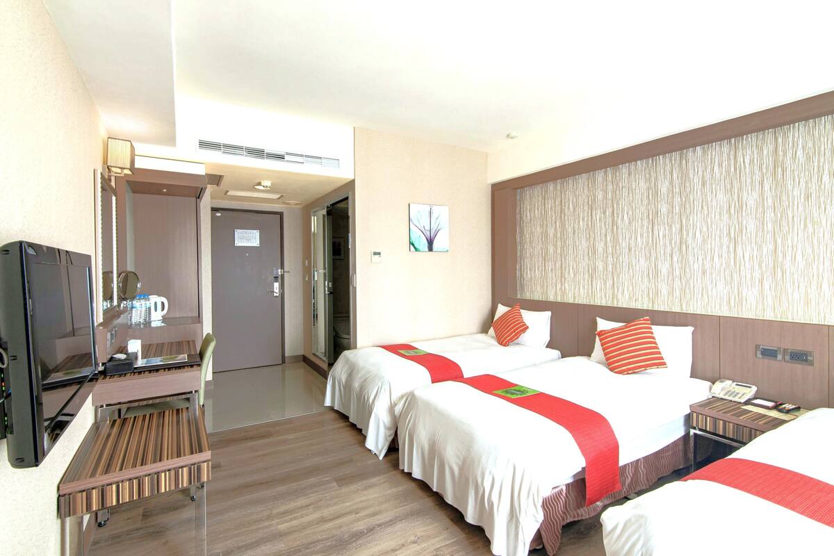 Une chambre d’hôtel avec deux lits, un bureau, une télévision et une porte de salle de bain.