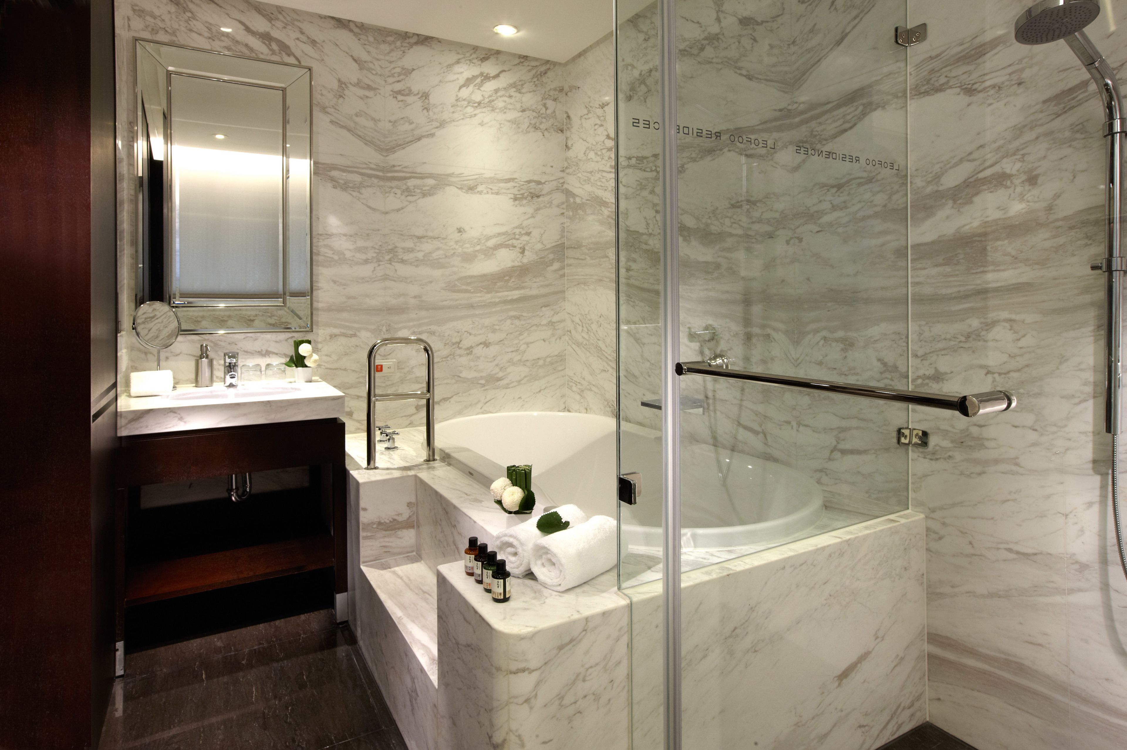 Un baño moderno con pared de mármol, un espejo grande, una bañera y una zona de ducha con mampara de cristal.