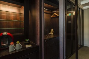 Habitación de hotel con detalles en madera oscura, un minibar con cafetera y un espejo con marco de madera.