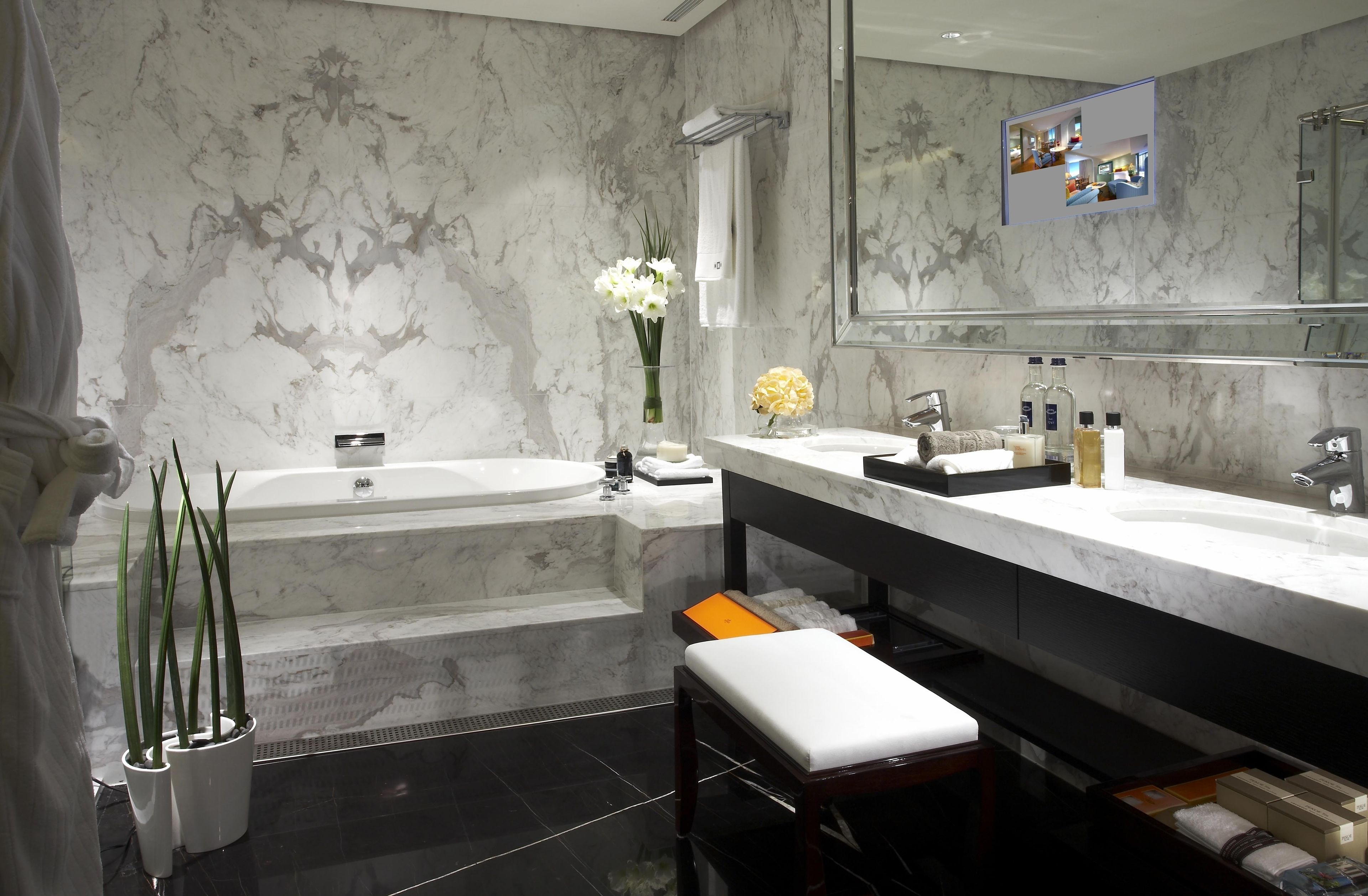 A modern bathroom with a marble wall, a bathtub, a vanity with a mirror, and a bench.