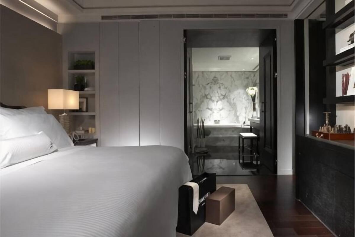 Une chambre d’hôtel avec un grand lit, une table de chevet, un bureau, une chaise, une salle de bain avec une baignoire et un lavabo.