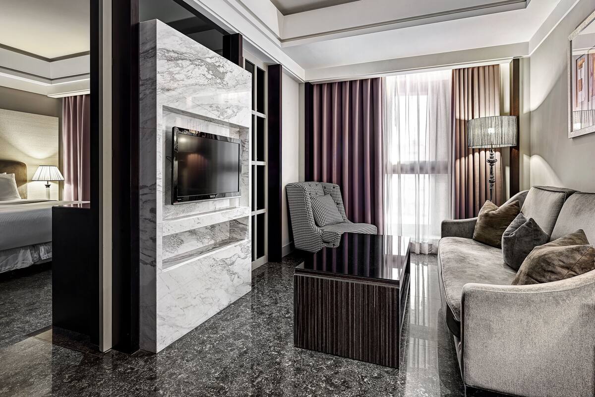 Une chambre d’hôtel moderne avec un mur en marbre, un téléviseur à écran plat, un canapé, un fauteuil et une table basse.