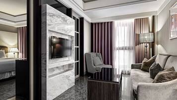 A modern hotel room with a marble wall, a flat-screen TV, a sofa, a chair, and a coffee table.